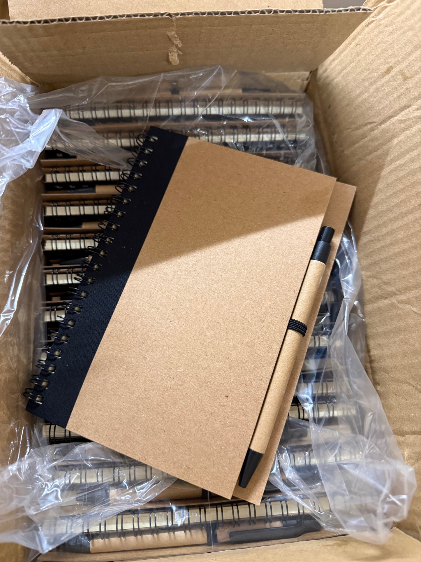 Box of 50 eco spiral A6 notebooks featuring a pen