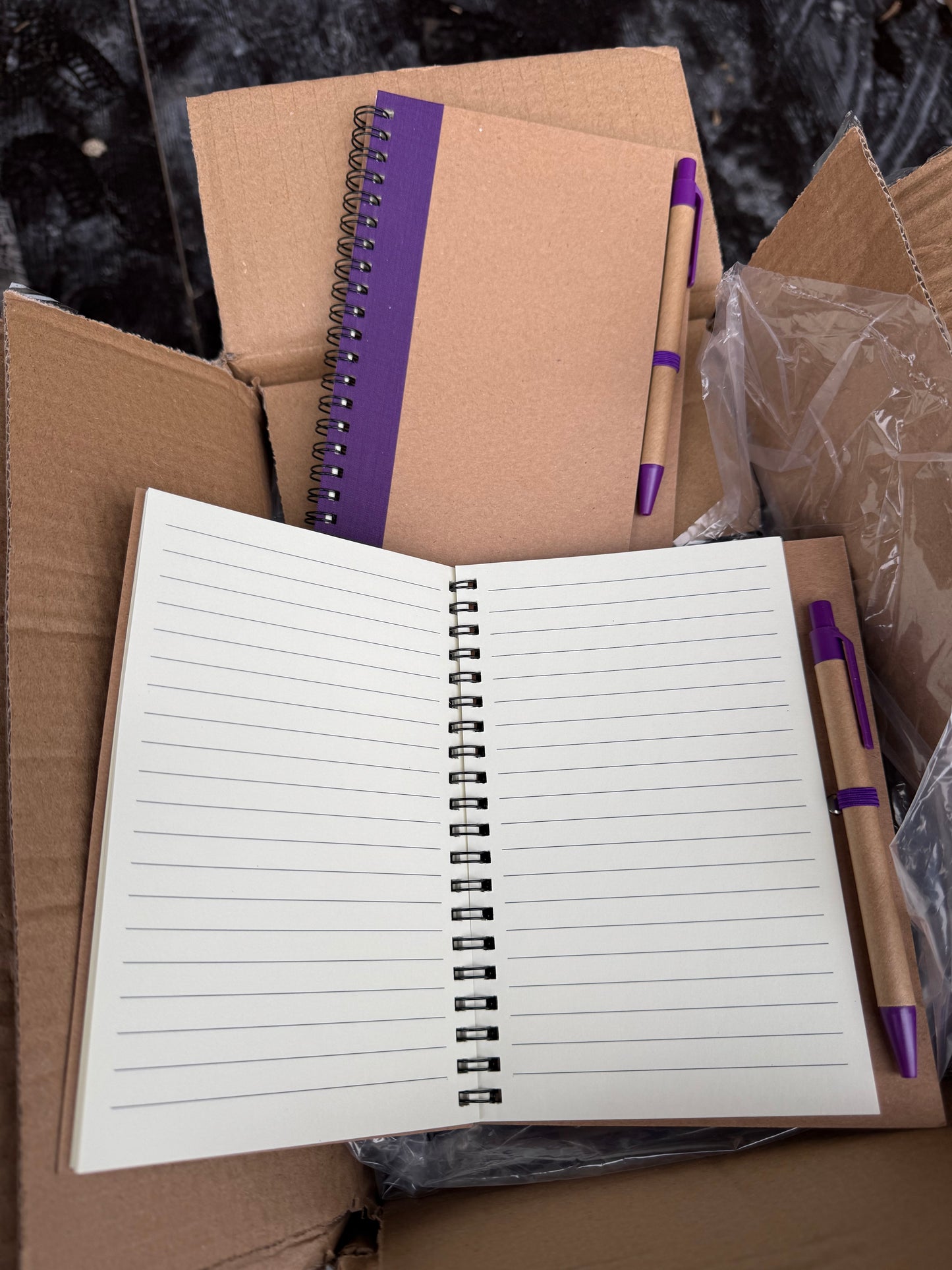 Box of 50 eco spiral A6 notebooks featuring a pen