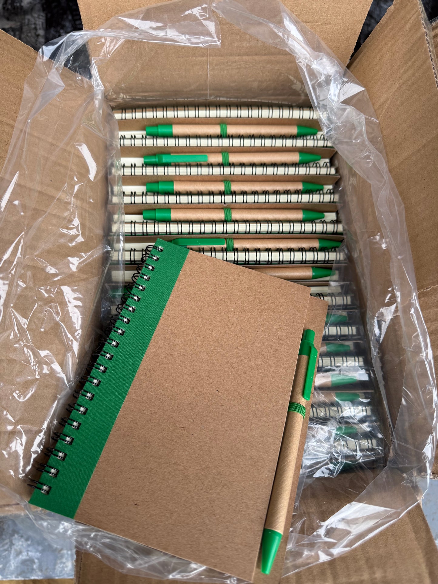 Box of 50 eco spiral A6 notebooks featuring a pen