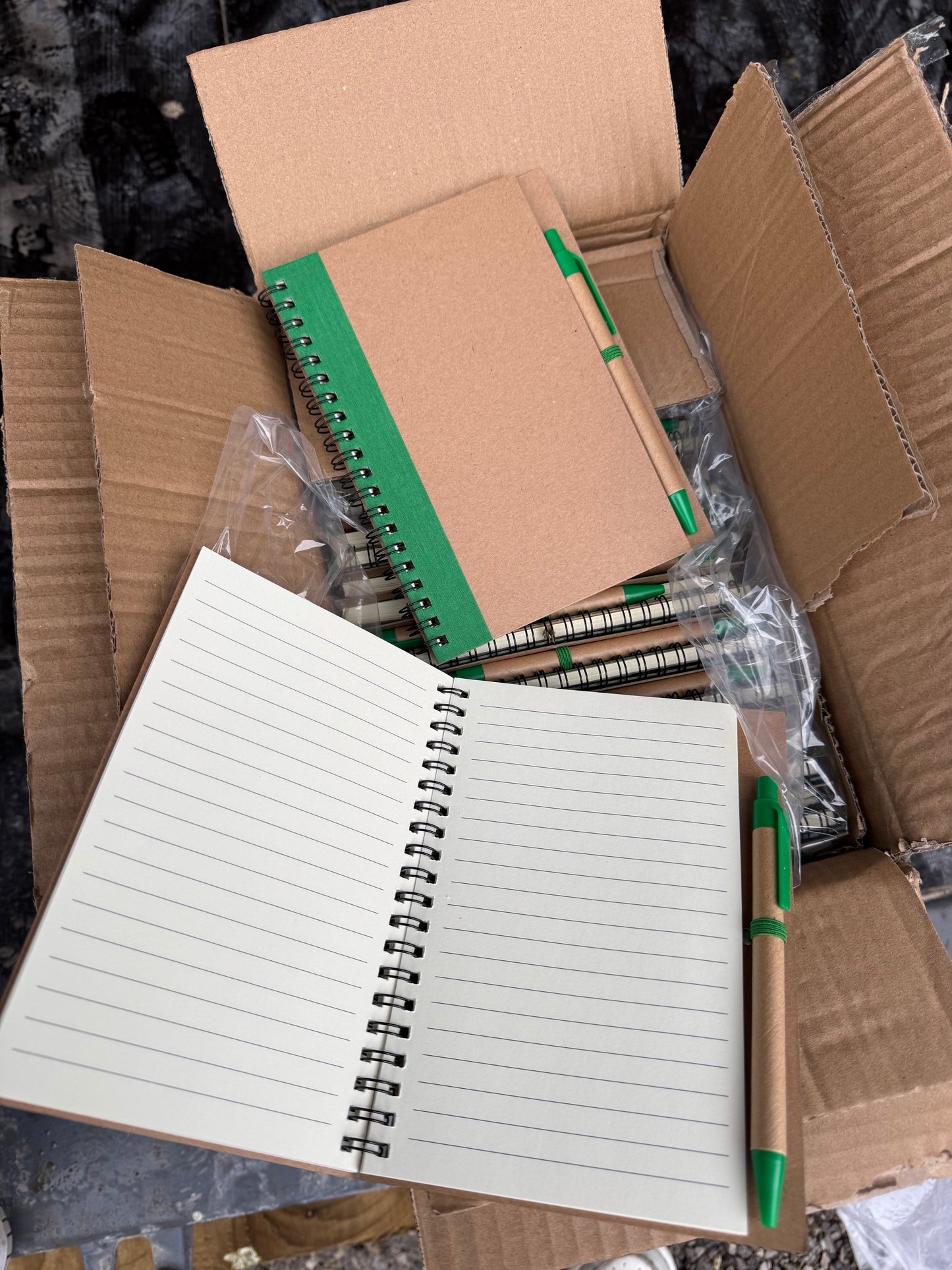 Box of 50 eco spiral A6 notebooks featuring a pen