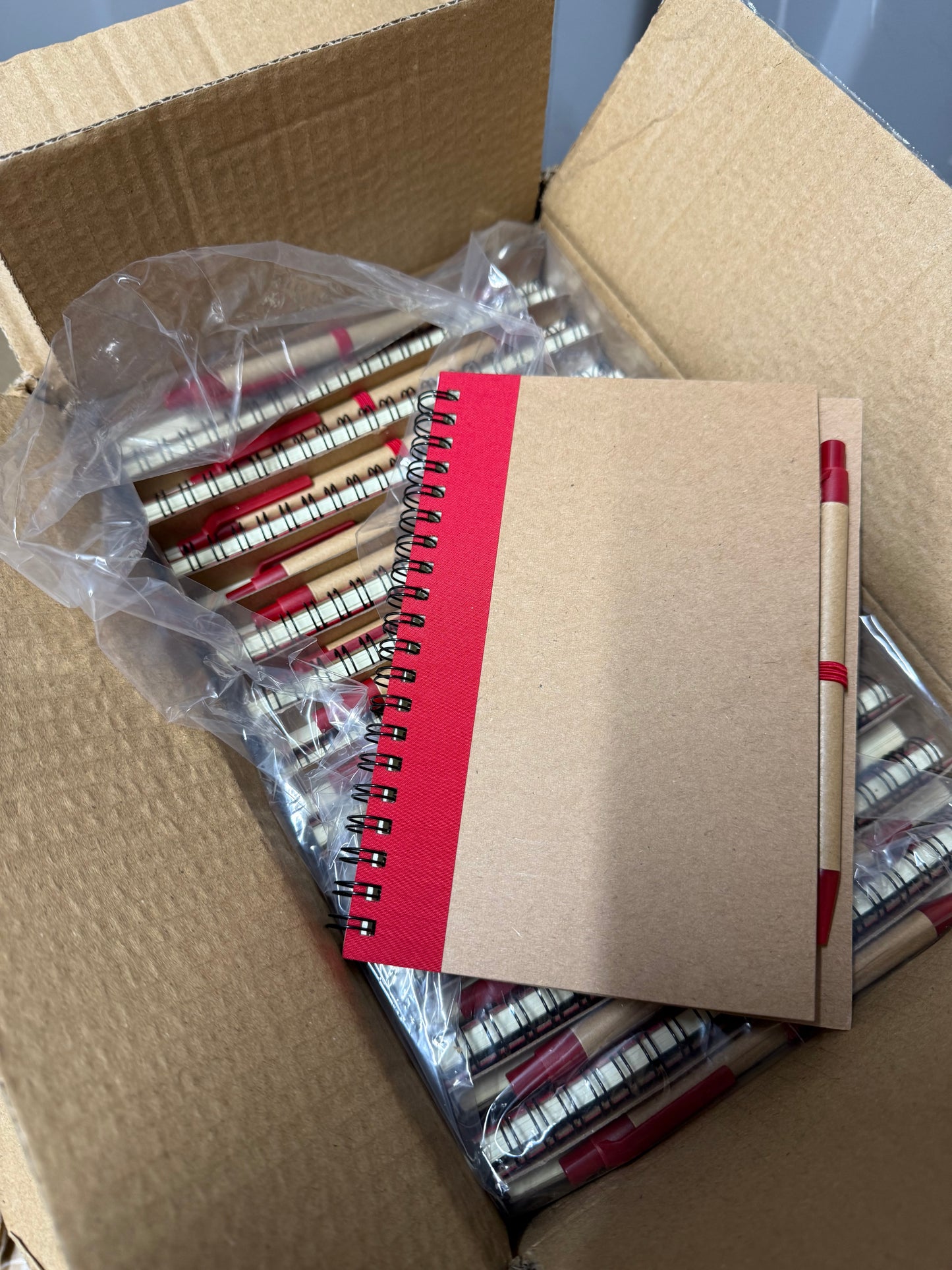 Box of 50 eco spiral A6 notebooks featuring a pen