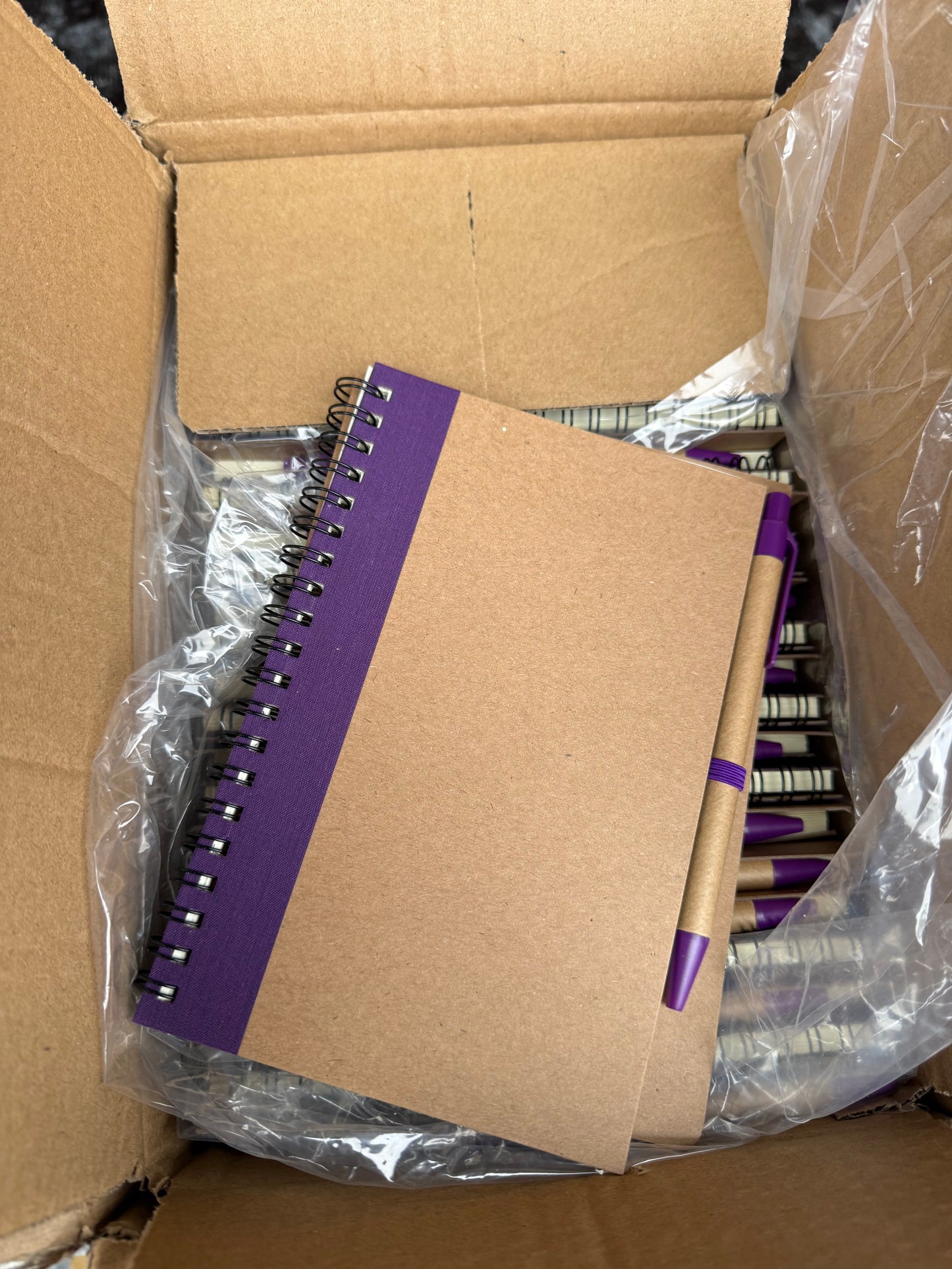 Box of 50 eco spiral A6 notebooks featuring a pen